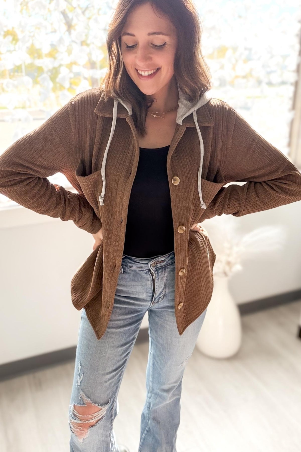 Woman wearing a brown camel jacket and blue jeans indoors