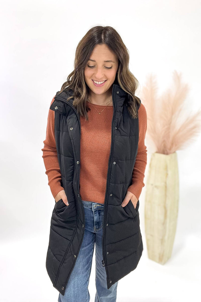 Woman wearing a black puffer vest over a copper shirt with a white background