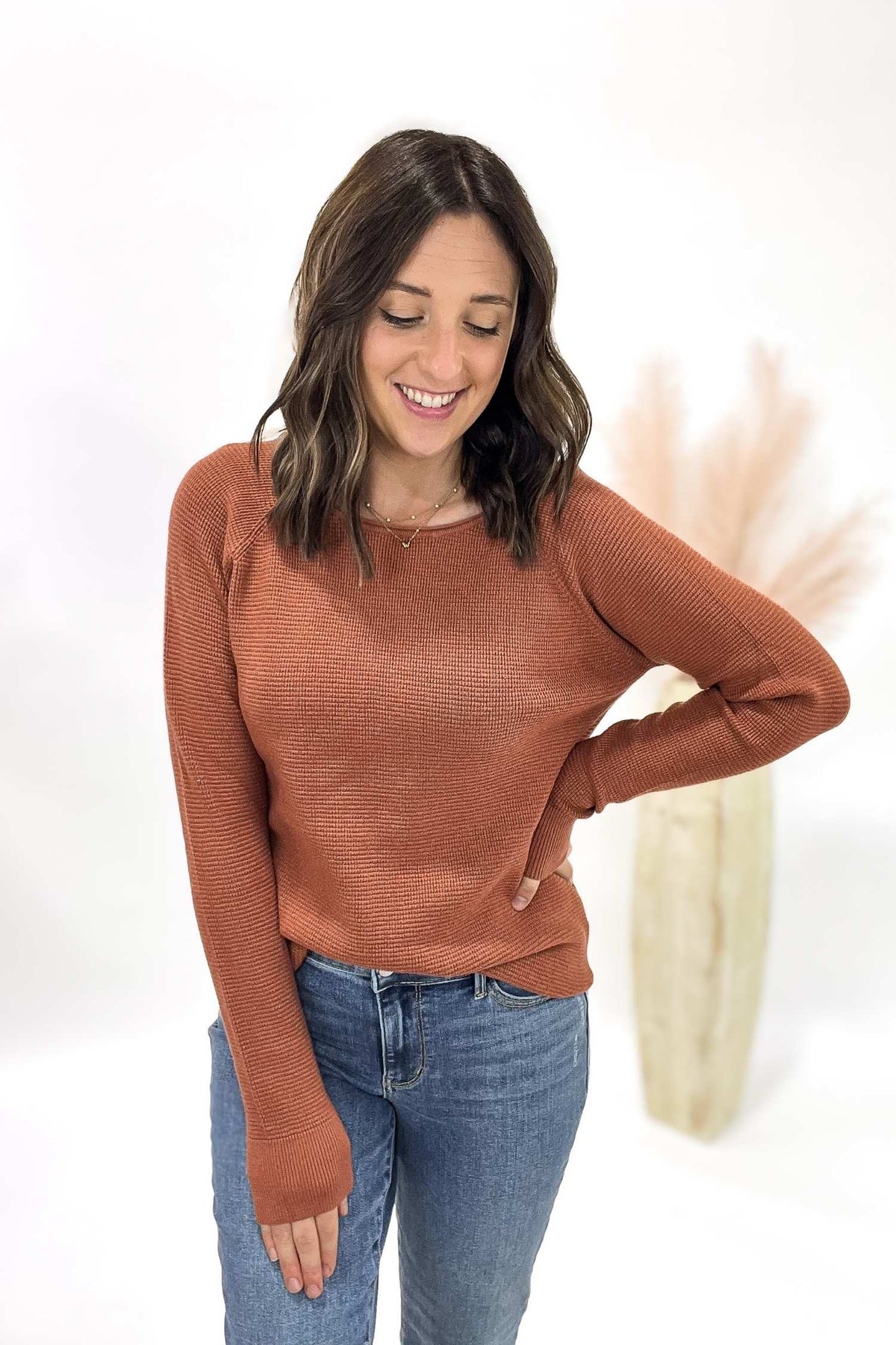 Woman wearing a copper sweater and blue jeans on a white background