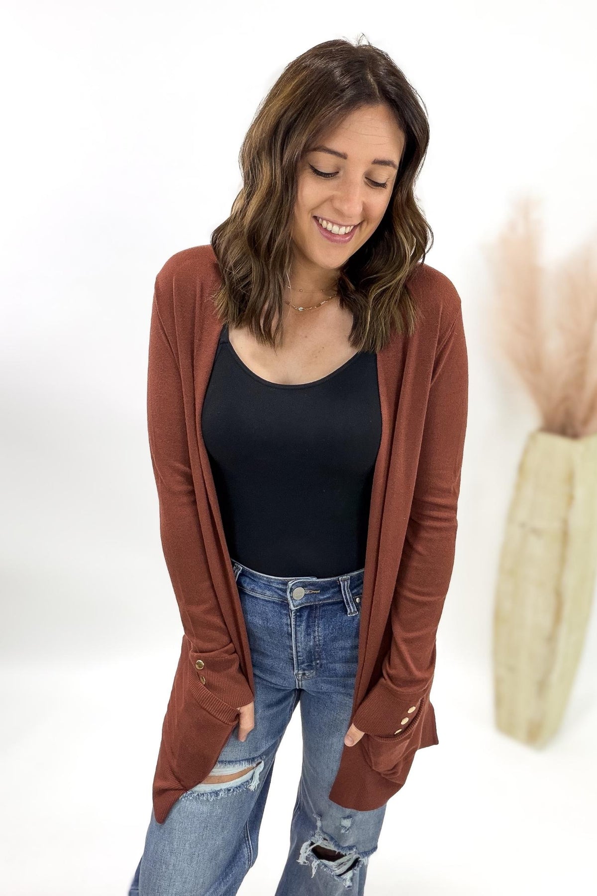 Woman wearing a copper cardigan, black top, and blue jeans on a white background
