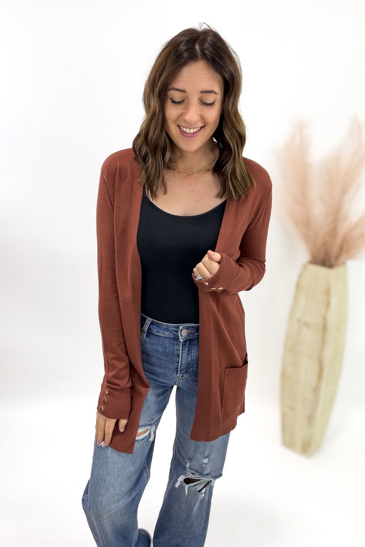 Woman wearing a copper cardigan over a black top and blue jeans on a white background