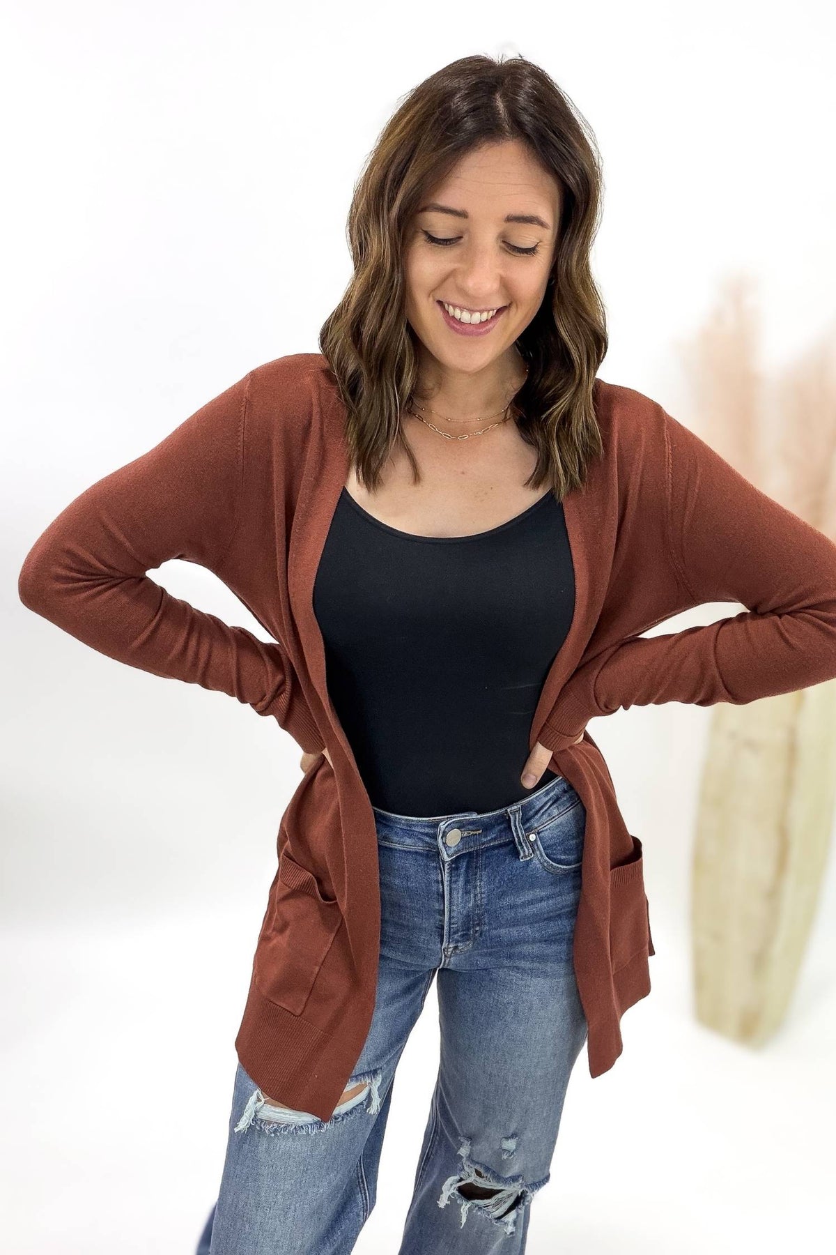 Woman wearing a copper cardigan, black top, and blue jeans on a white background