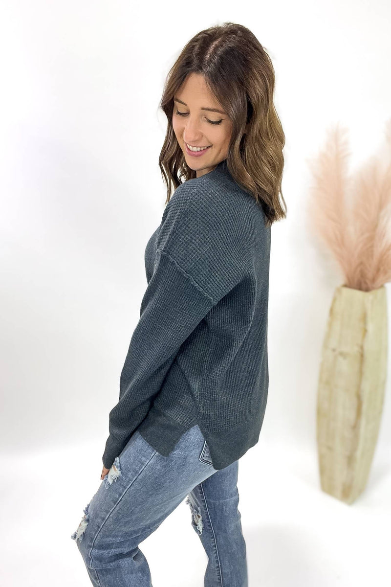 Woman wearing a dark teal sweater and jeans against a white background