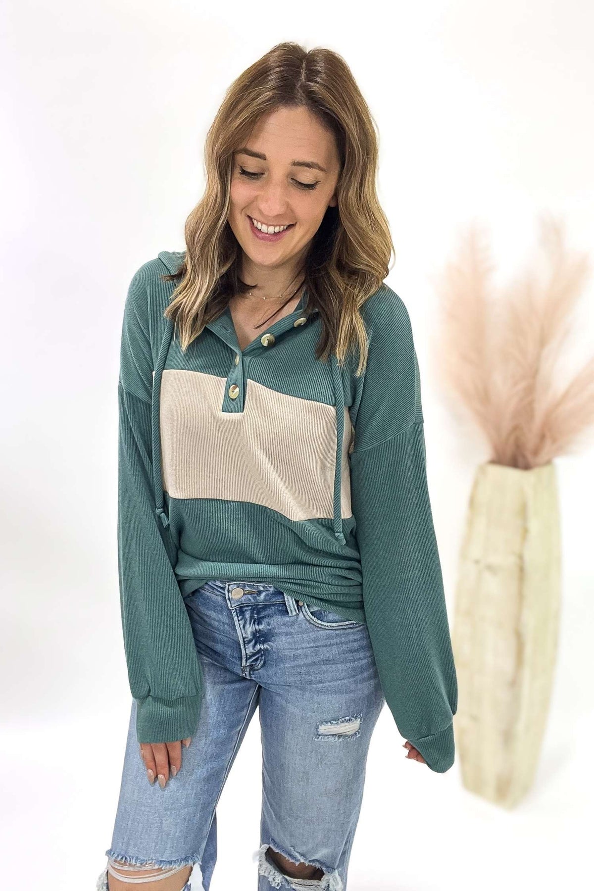 Woman wearing a teal and beige long-sleeve top with blue jeans on a white background