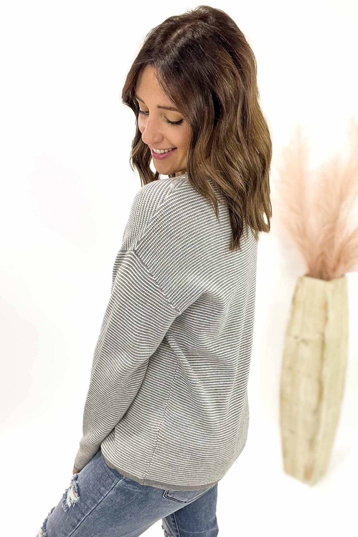 Woman wearing a gray striped sweater and blue jeans on a white background