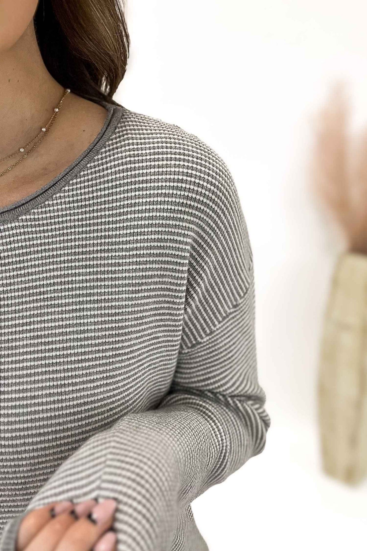 Person wearing a gray long-sleeve striped sweater with a blurred background