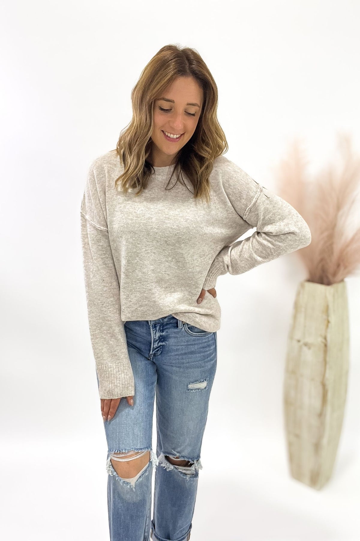 Woman wearing a light gray sweater and ripped jeans on a white background