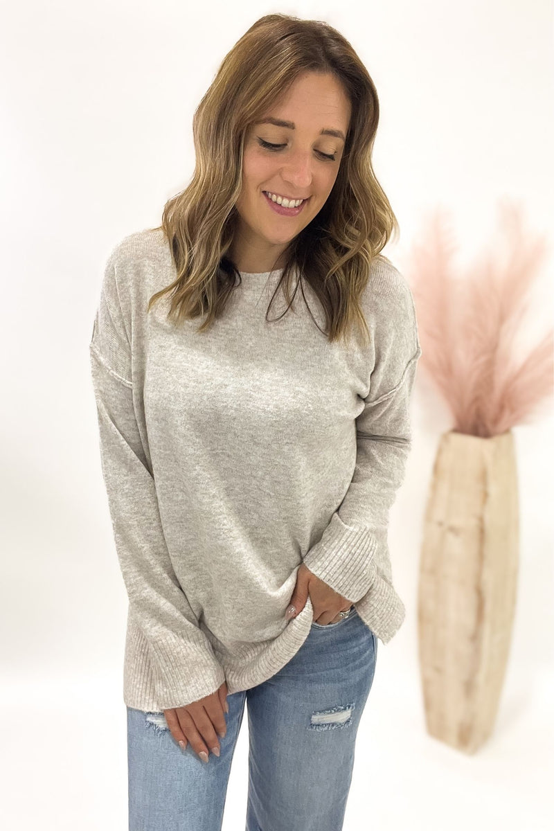 Woman wearing a oatmeal sweater and blue jeans on a white background