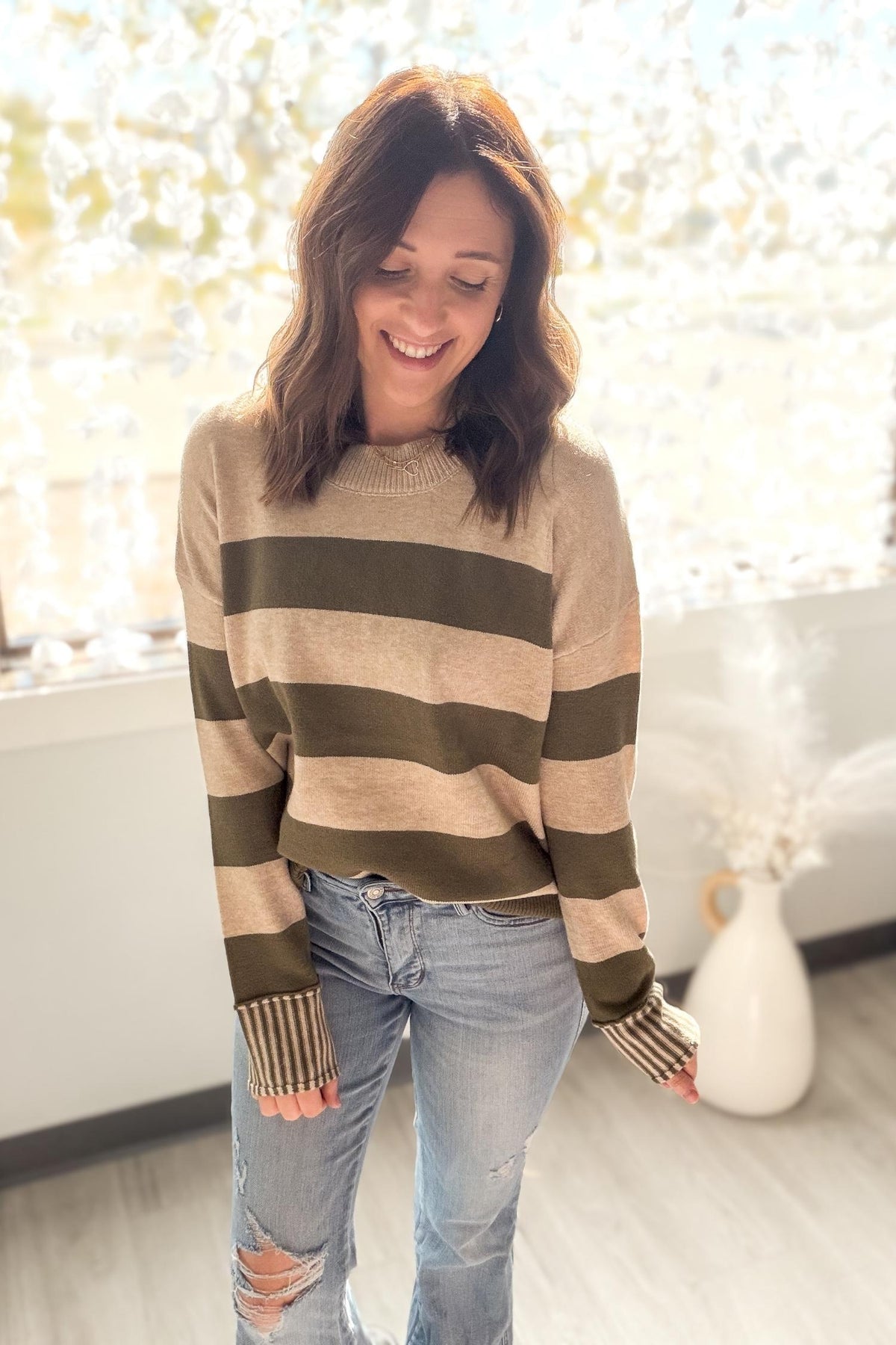 Woman wearing a striped sweater and jeans indoors with a blurred background