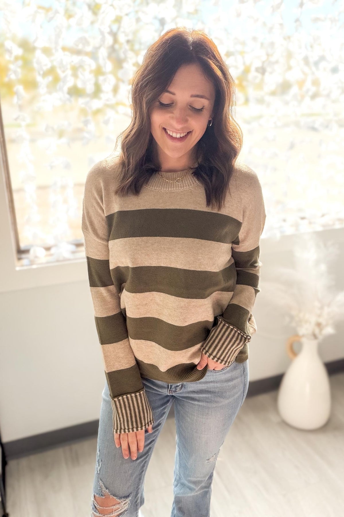 Woman wearing a striped sweater and jeans indoors with a window in the background