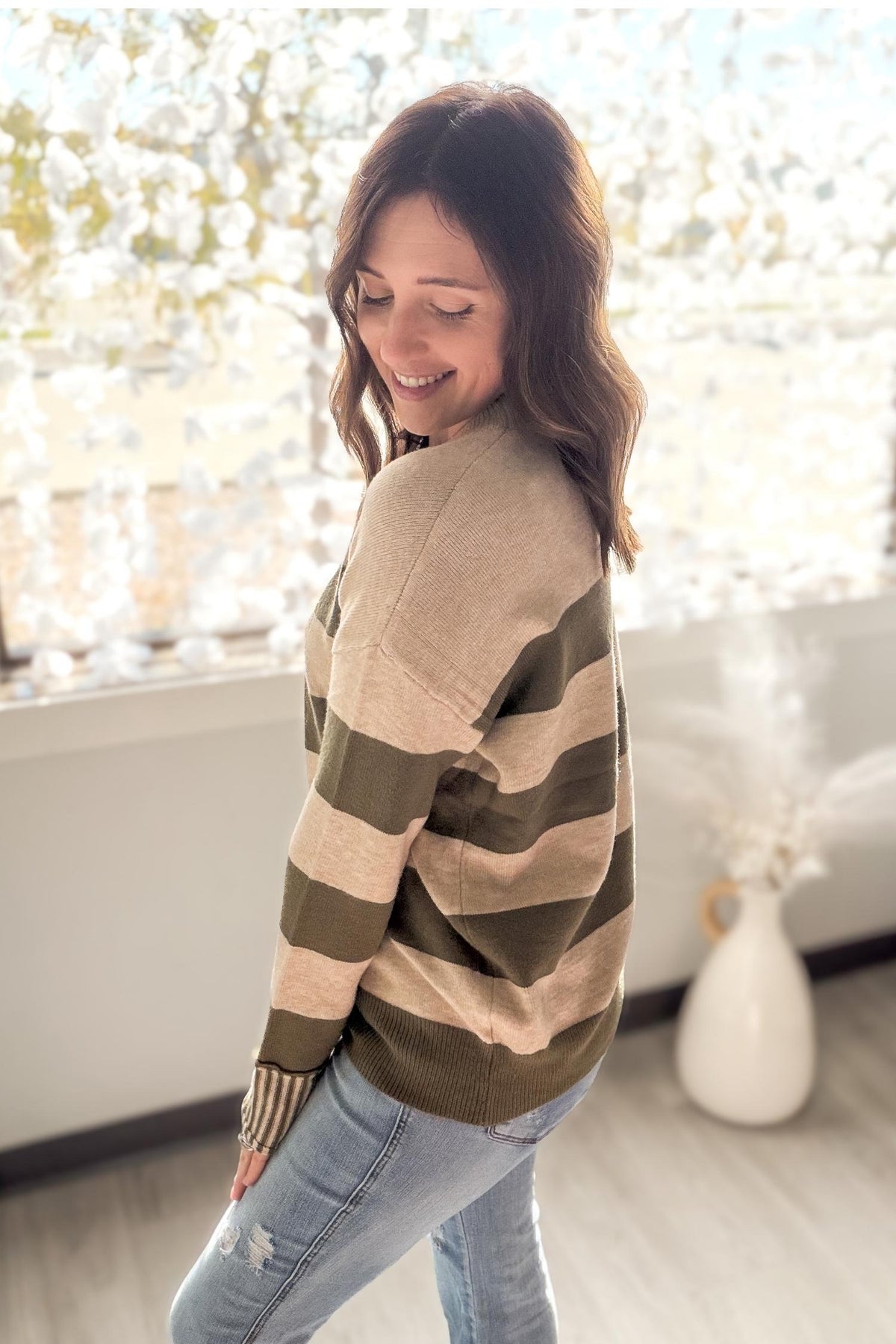 Woman wearing a striped sweater and jeans in a room with decorative lights.