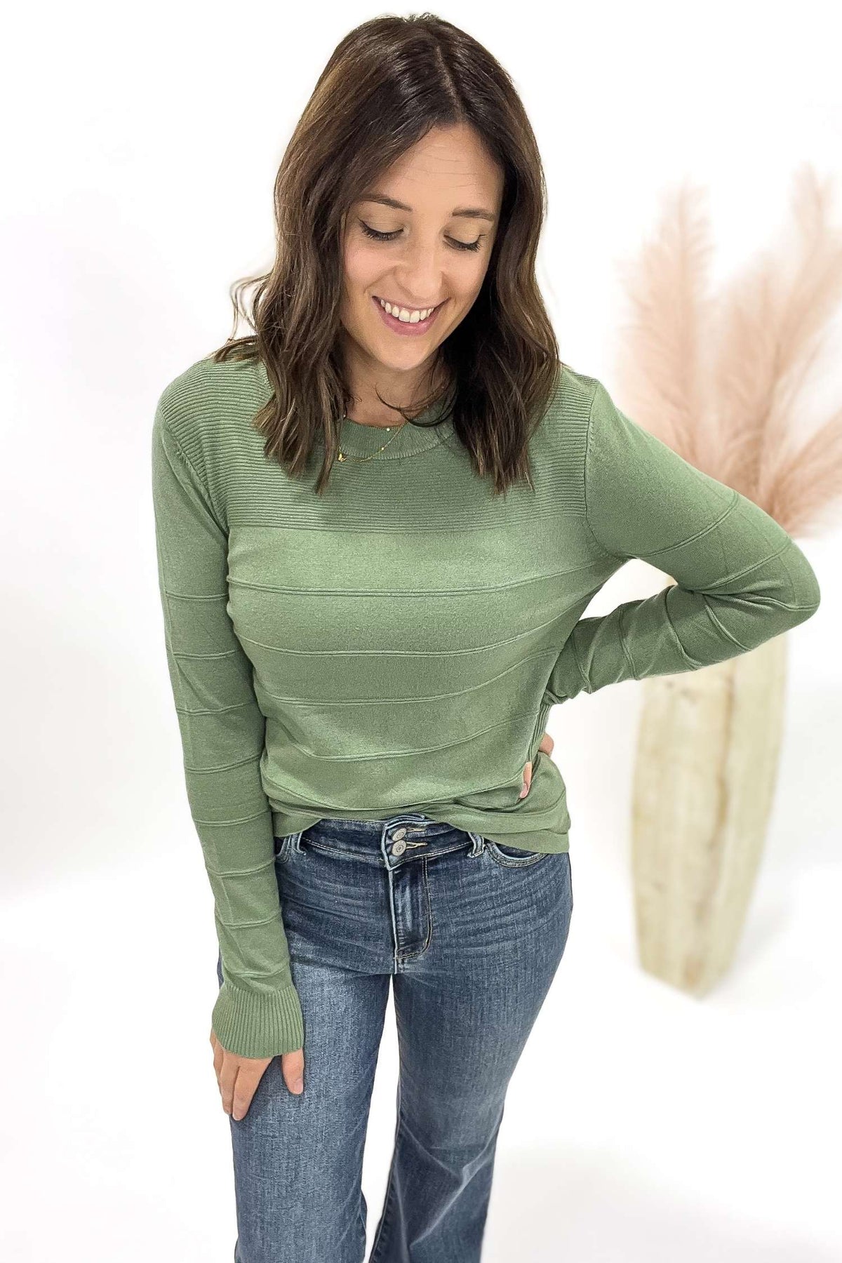 Woman wearing a green sweater and blue jeans on a white background