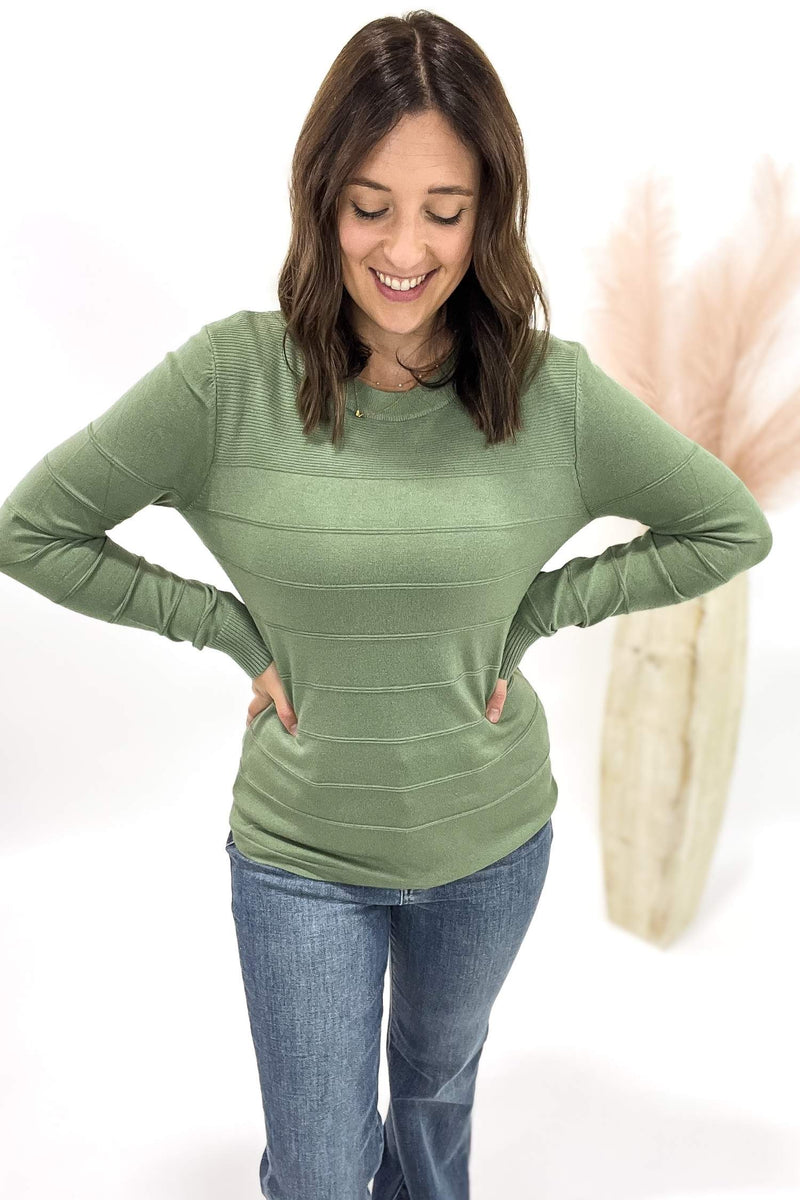 Woman wearing a green long-sleeve top and blue jeans on a white background