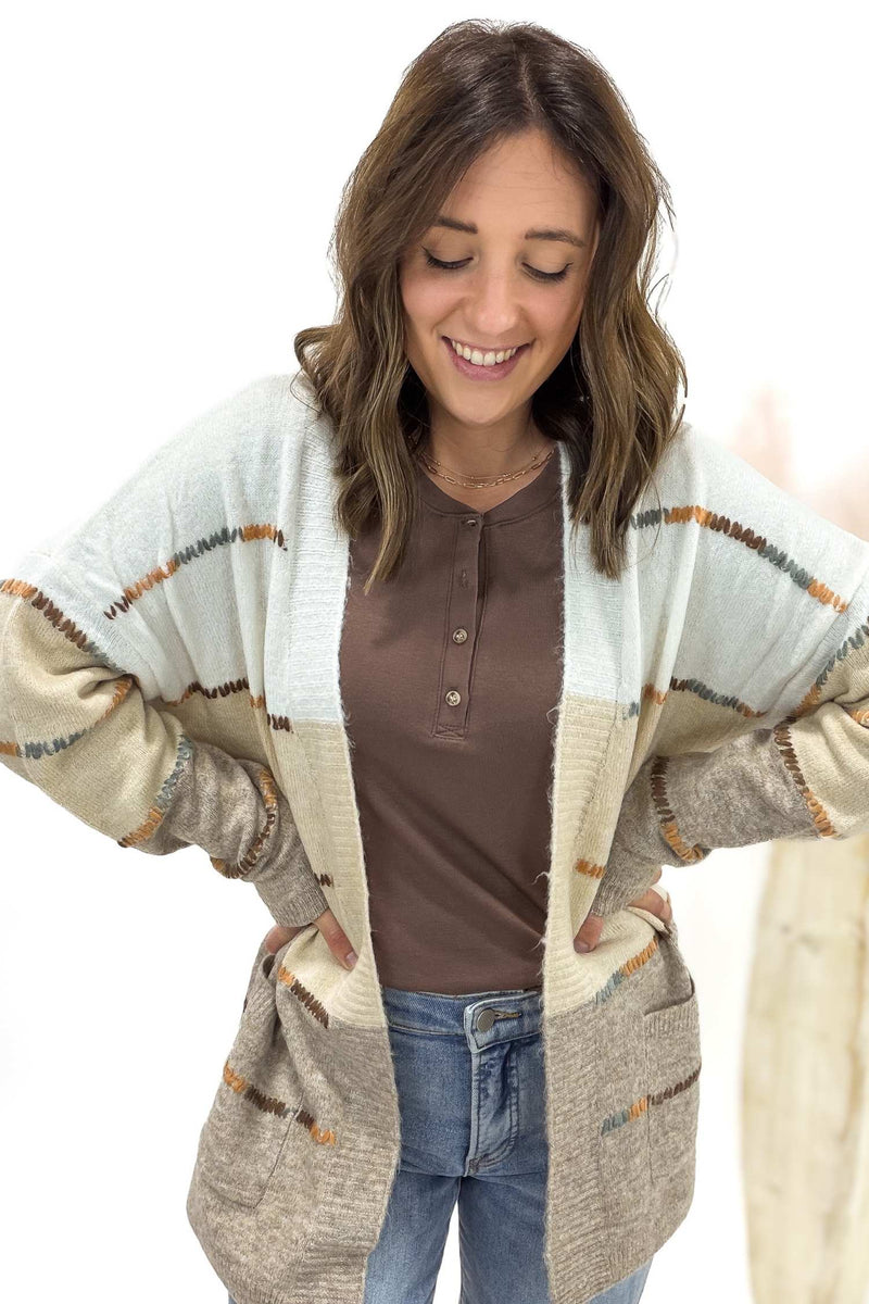 Woman wearing a patterned cardigan over a brown shirt and jeans on a white background