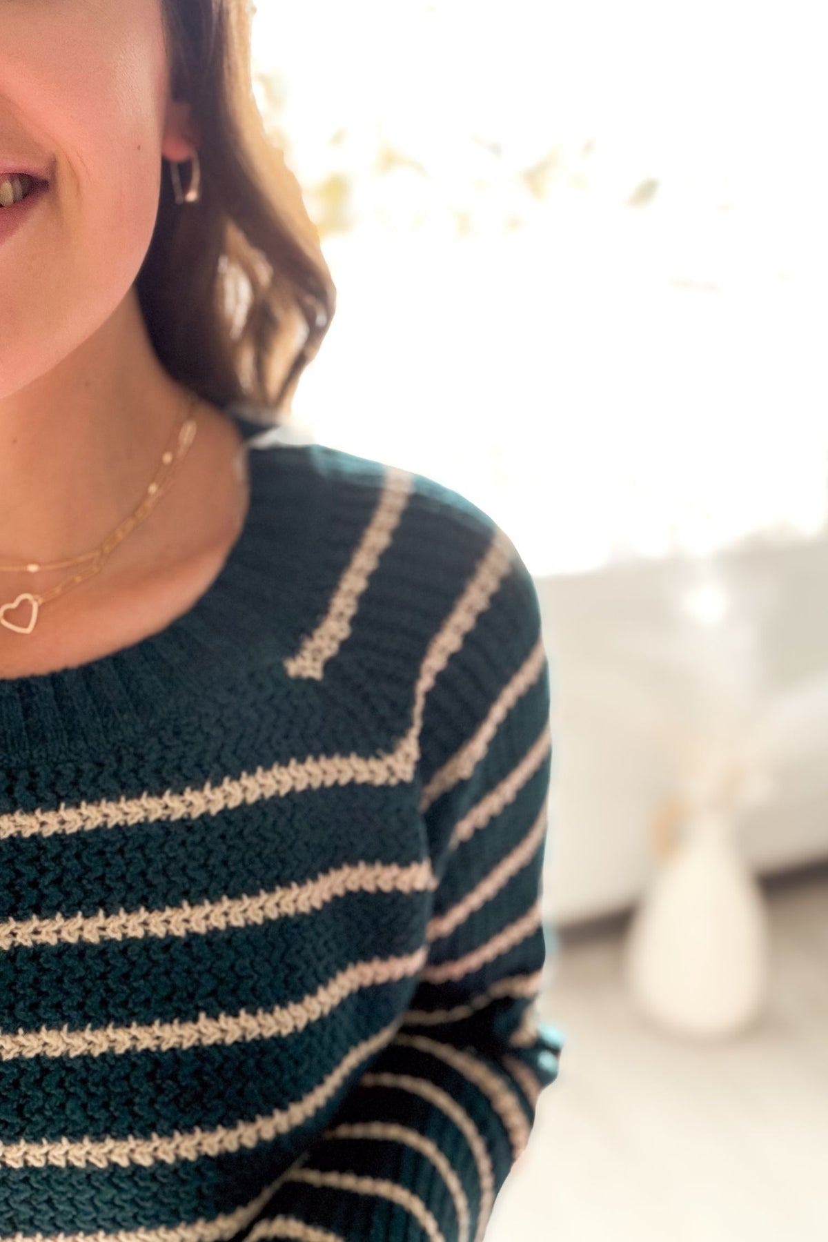 Person wearing a dark green and beige striped sweater with a blurred background