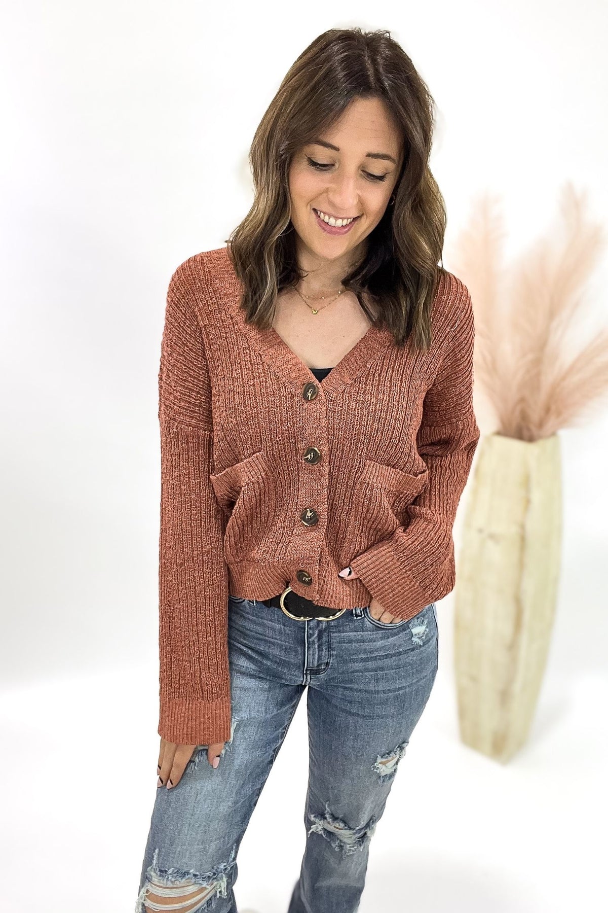 Woman wearing a terracotta cardigan with jeans and a white background