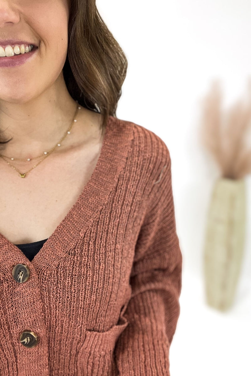 Woman wearing a terracotta cardigan with jeans and a white background