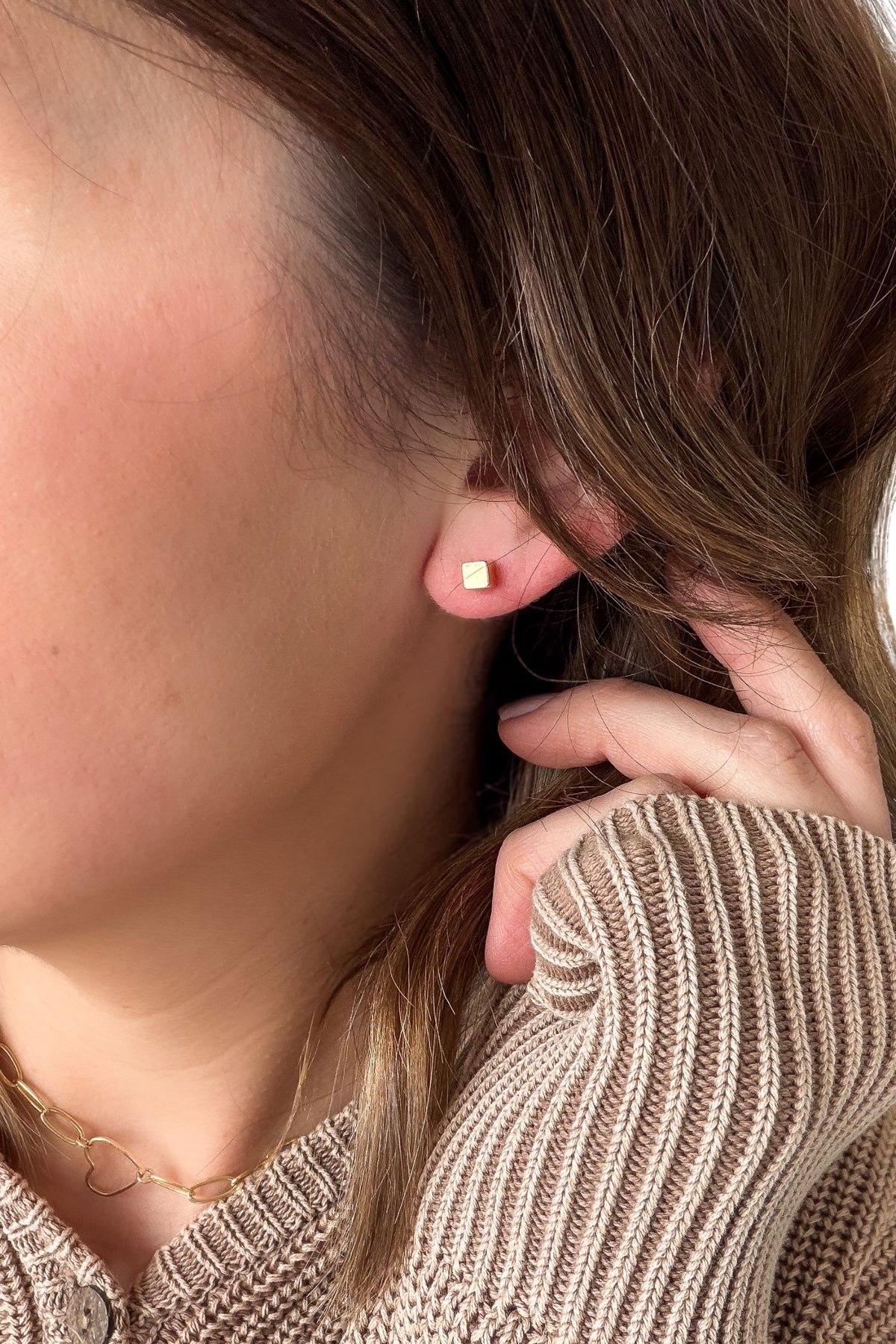 Close-up of a person wearing a gold earring with a neutral background