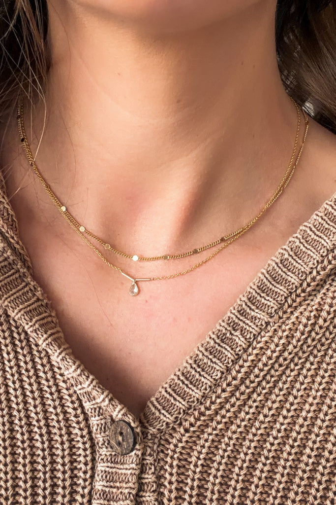 Close-up of a person wearing a gold necklace with a textured brown cardigan.