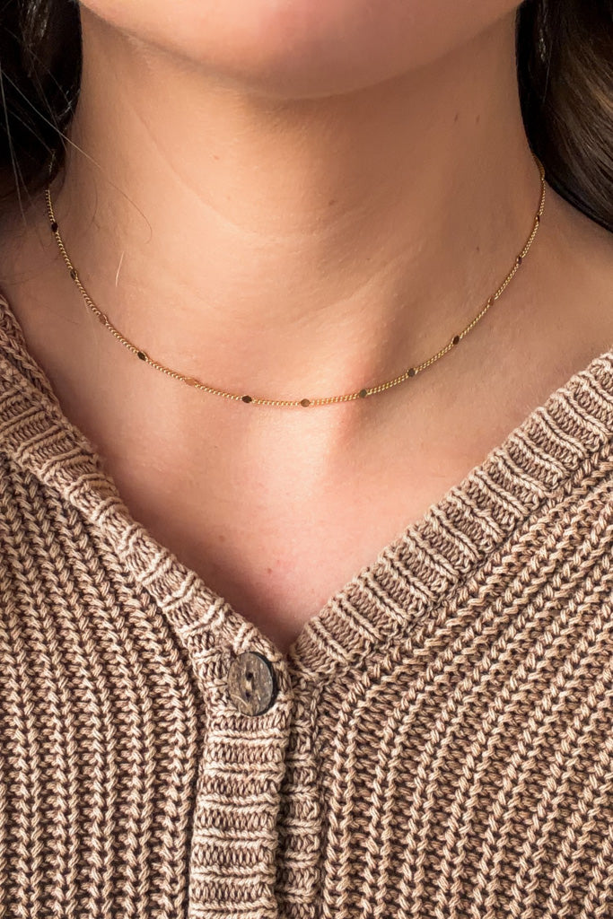 gold necklace with small flat dots worn by a person in a textured brown sweater.