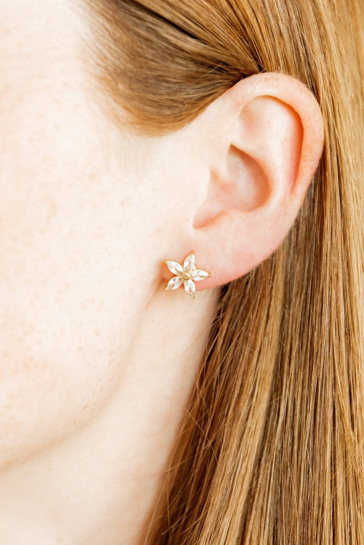 Close-up of an ear wearing a floral earring with blonde hair.