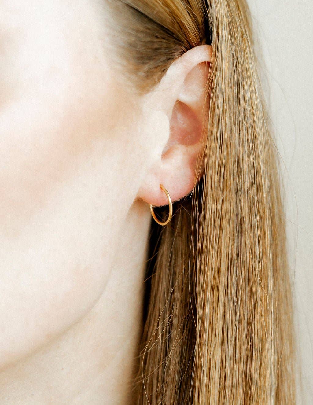 Close-up of a person wearing a gold hoop earring with a neutral background