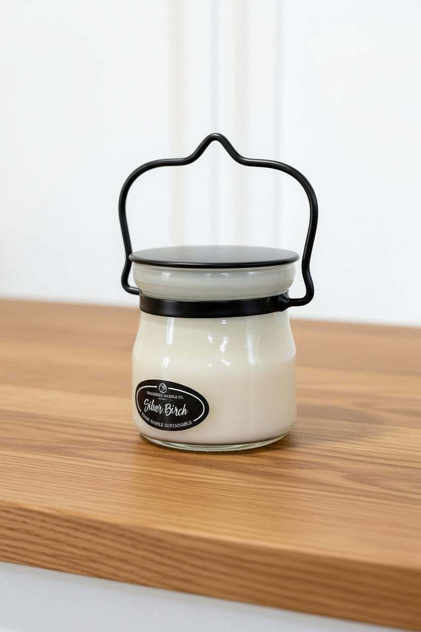 Small glass jar with black handle and lid, held by a hand on a white background