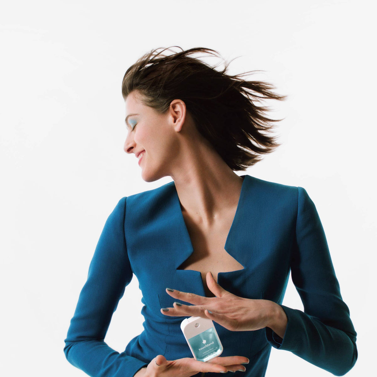 Woman in a blue suit holding a small bottle with a white label against a light gray background