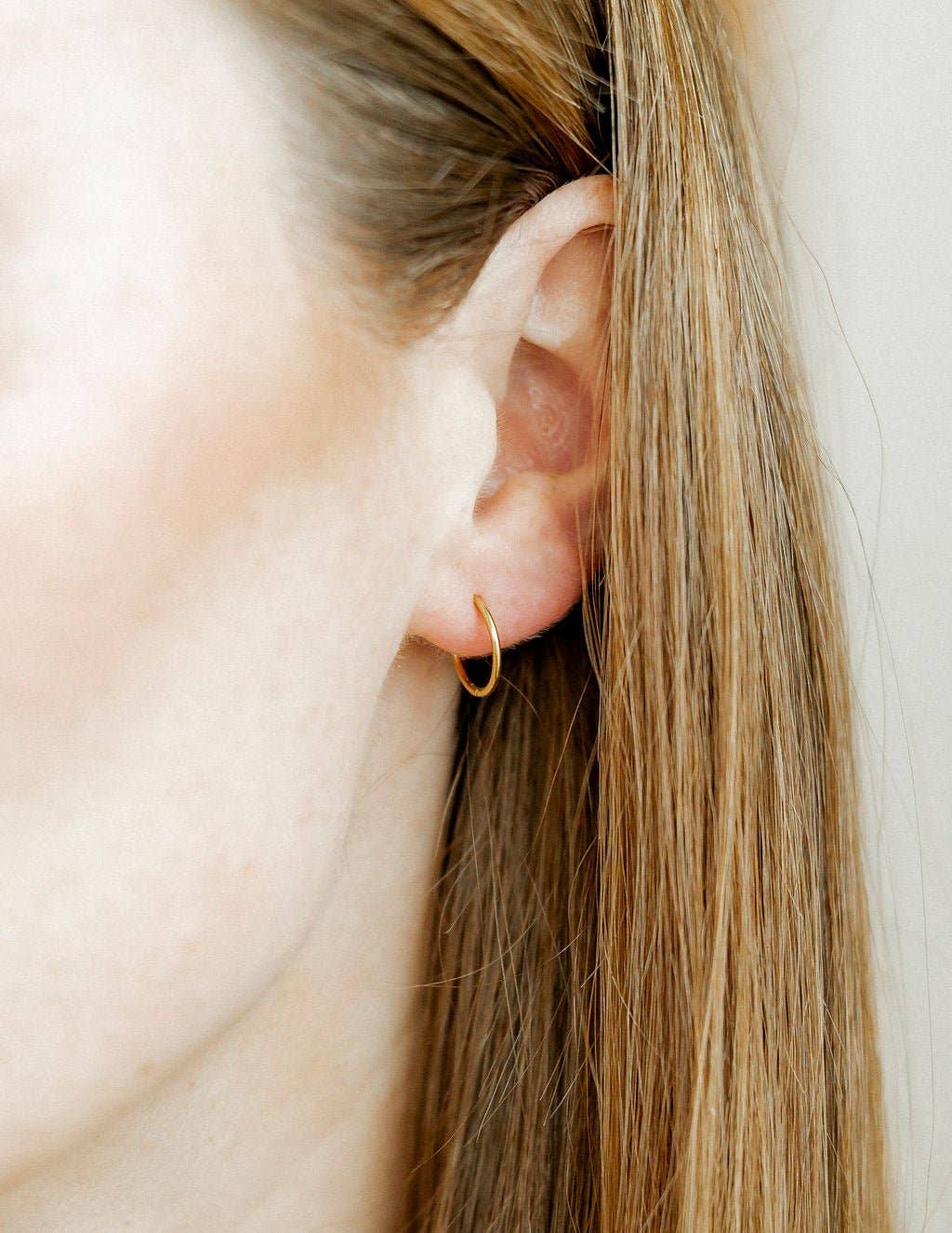 Close-up of a person wearing a gold hoop earring with a neutral background