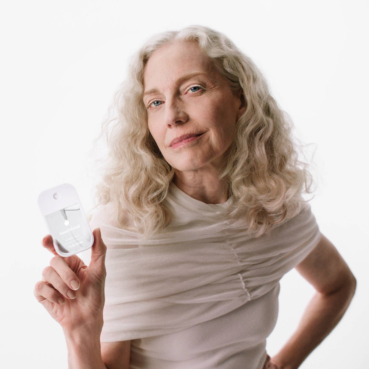 Woman holding touchland unscented handsantizer against a plain background