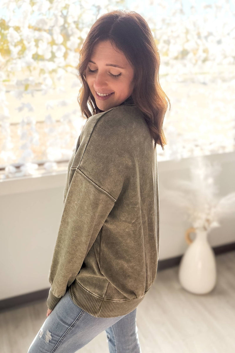 Woman wearing a olive sweatshirt in a softly lit room