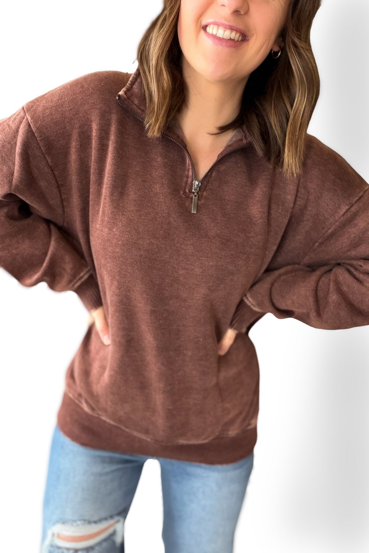 Woman wearing a brown zip-up sweatshirt and light blue jeans on a white background