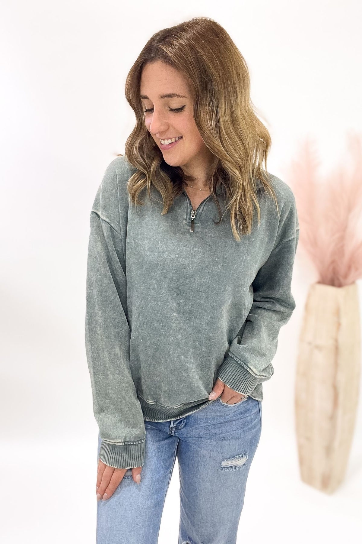 Woman wearing a jade acid-wash pullover and blue jeans on a white background