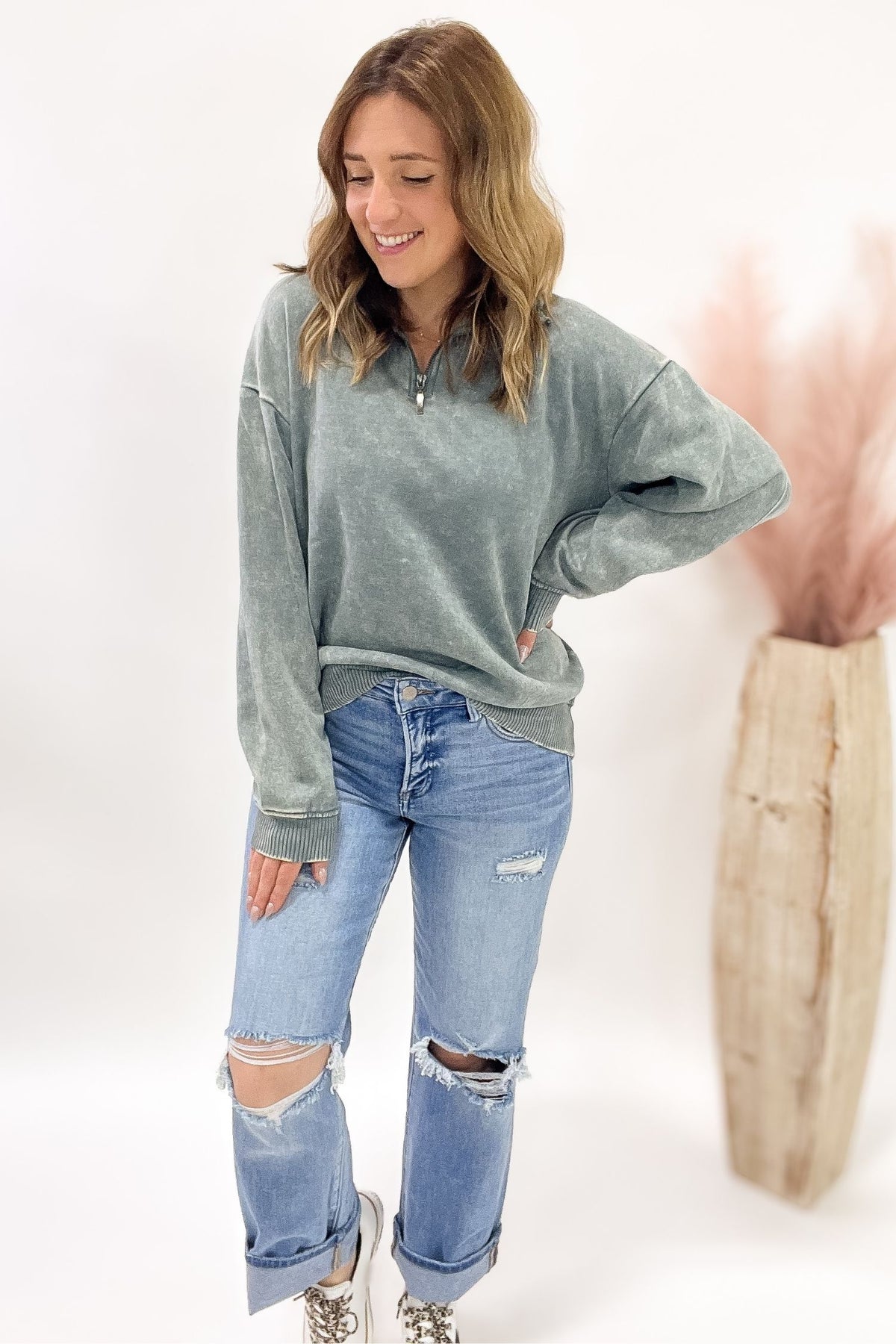 Woman wearing a jade oversized sweatshirt and ripped jeans on a white background