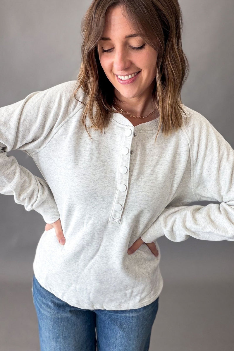 woman wearing a long sleeve heather ash grey snap button french terry pullover against a grey background.