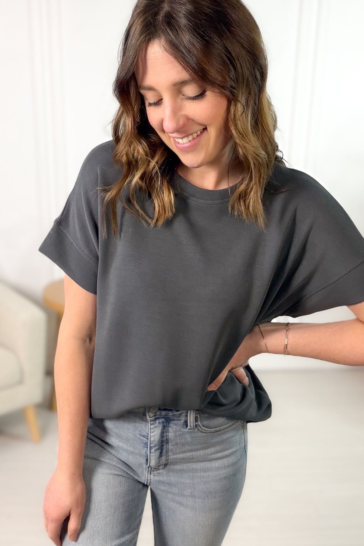 Woman wearing a dark gray t-shirt and light blue jeans indoors.