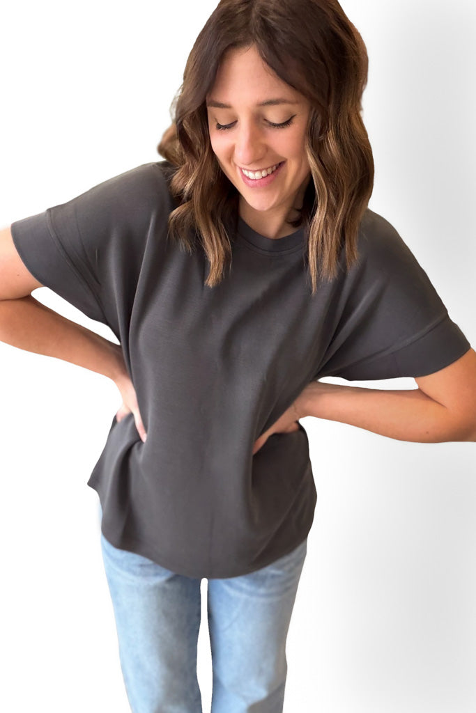 Woman wearing a dark gray t-shirt and light blue jeans on a white background