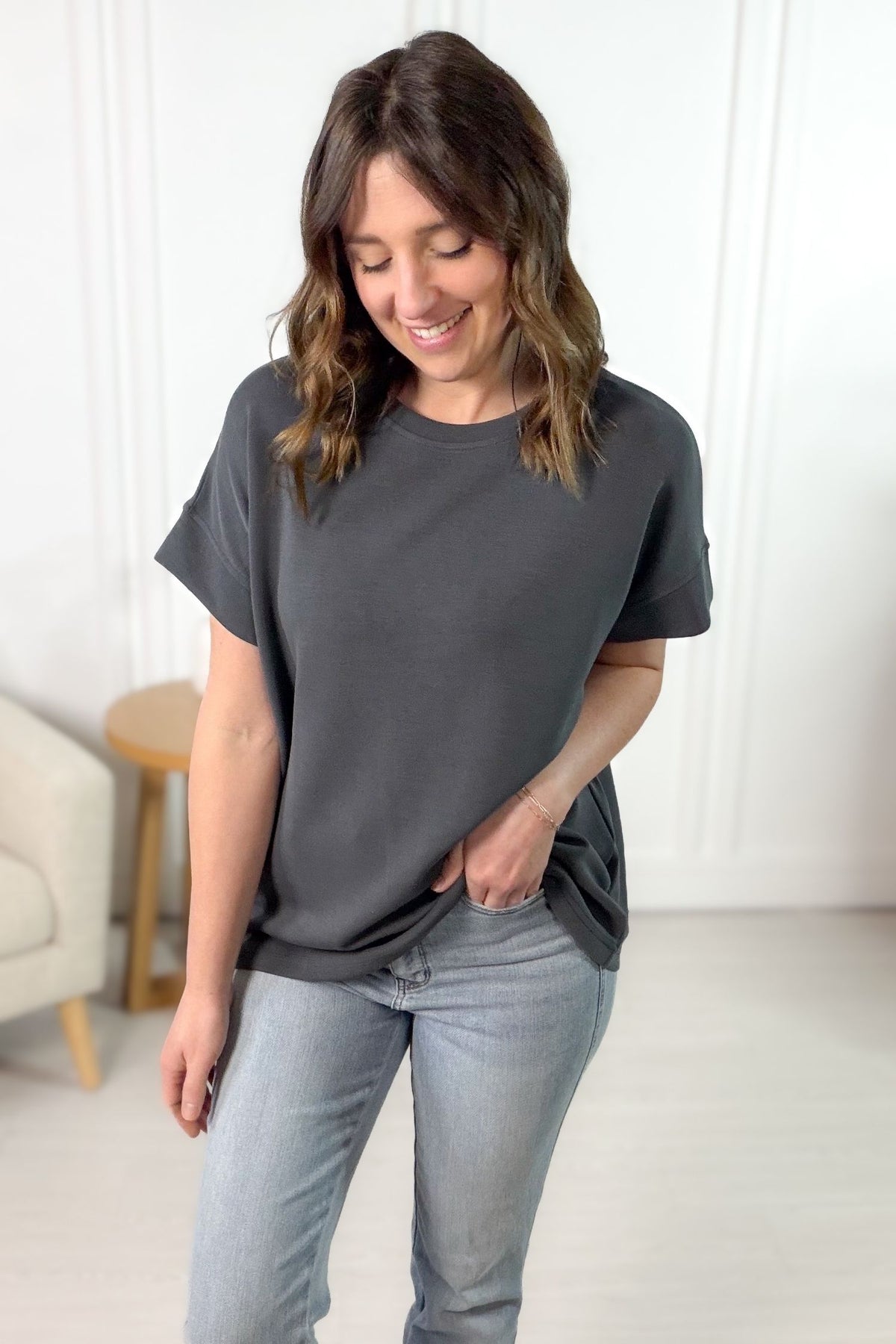 Woman wearing a gray t-shirt and jeans in a minimalistic room.