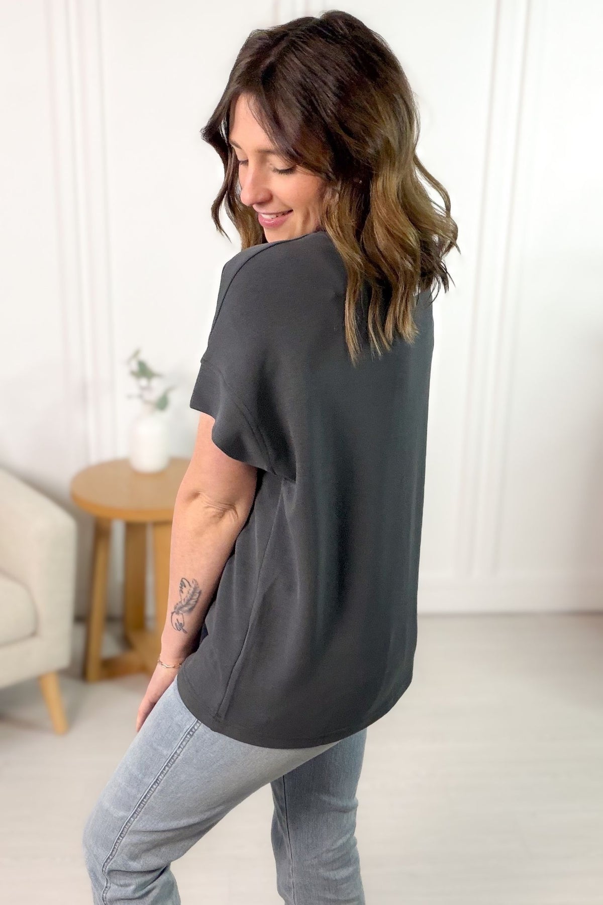 Woman wearing a dark gray t-shirt and light blue jeans in a minimalistic room.