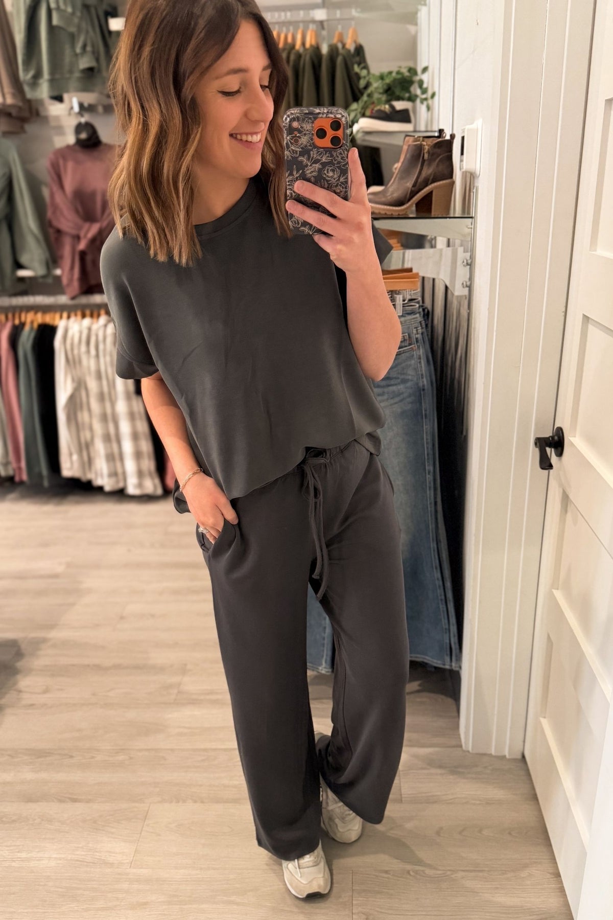 Woman taking a mirror selfie wearing a dark gray outfit set in a store.