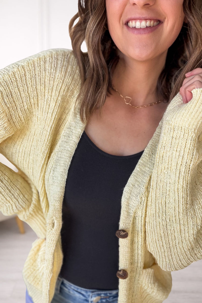 Woman wearing a yellow cardigan over a black top with a blurred background