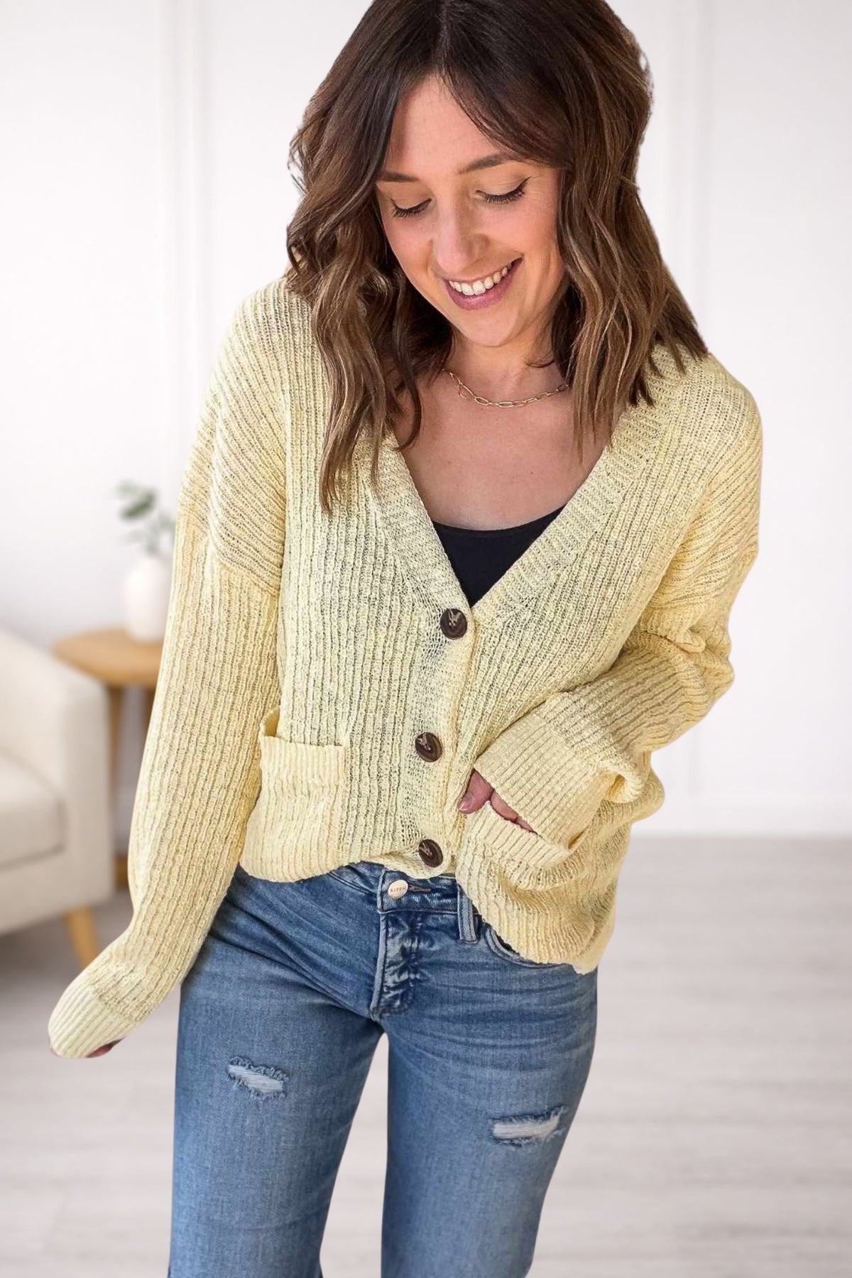 Woman wearing a yellow cardigan and blue jeans indoors.