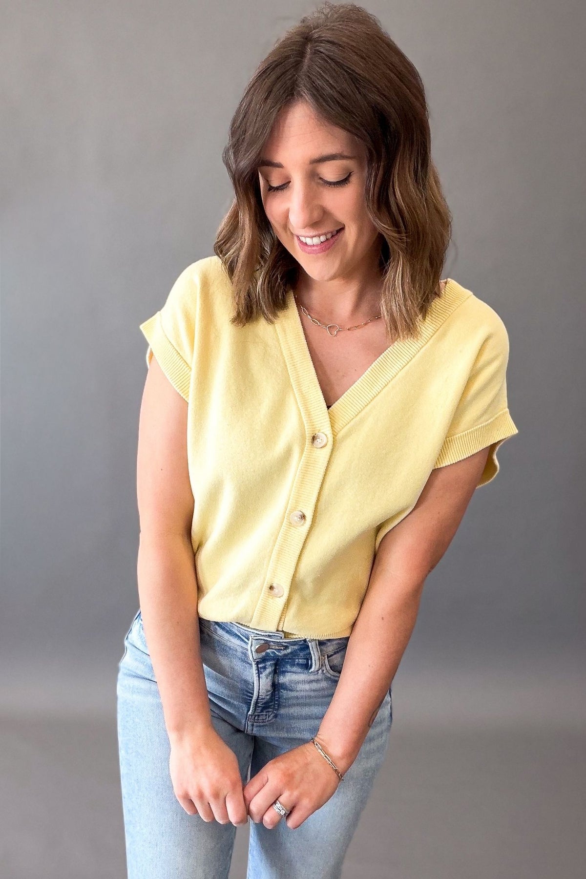 woman wearing a yellow button front cardigan with blue jeans on a grey background
