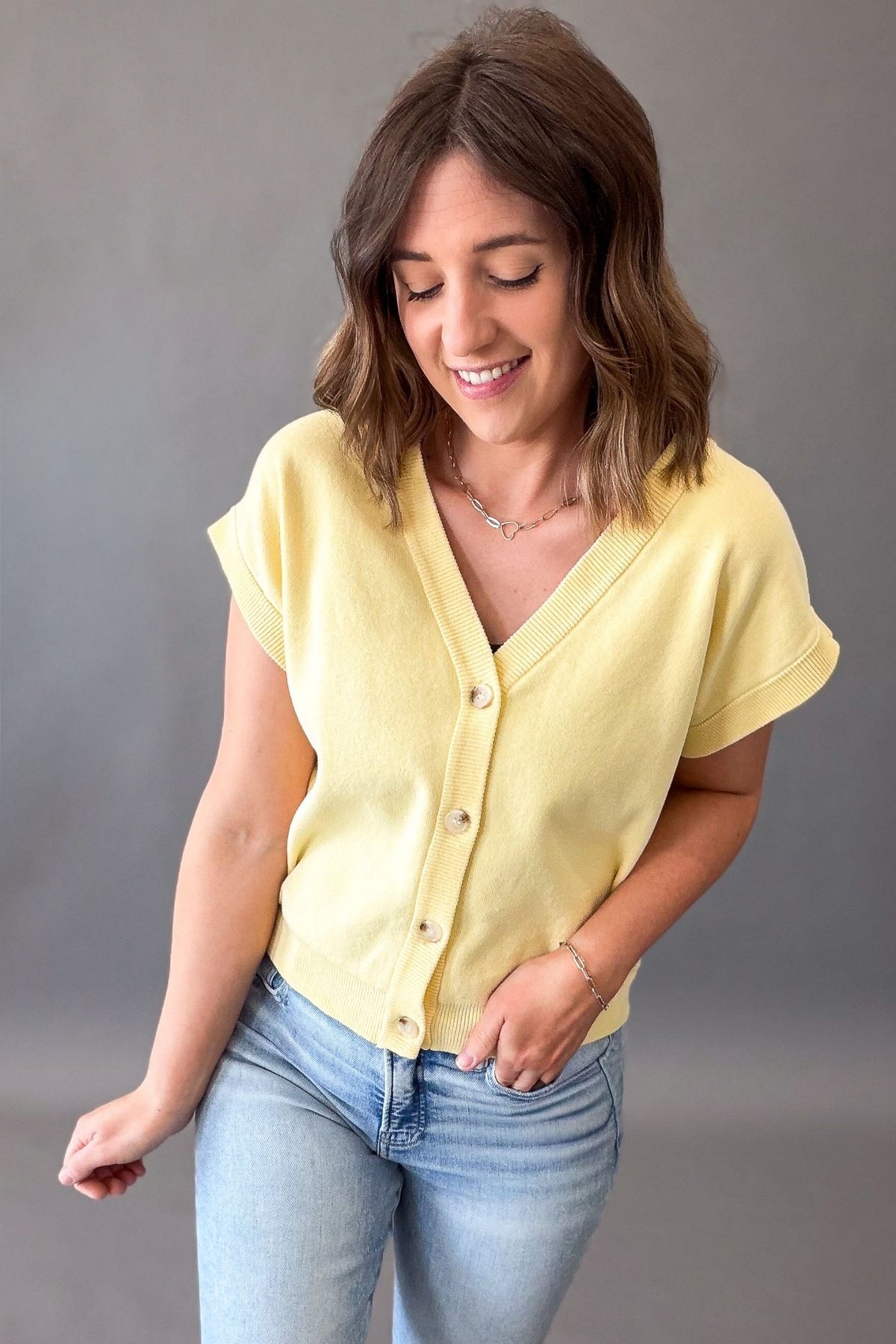 woman wearing a soft yellow button front cardigan with blue jeans on a grey background