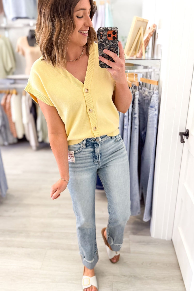 Woman taking a mirror selfie wearing a yellow cardigan and blue jeans in a clothing store.