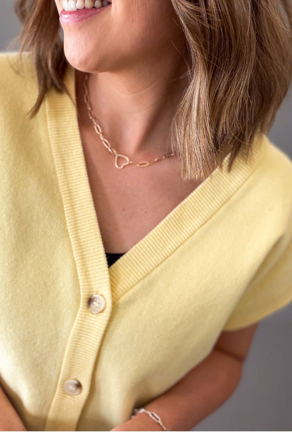 woman wearing a yellow button front cardigan with blue jeans on a grey background showing the close up details