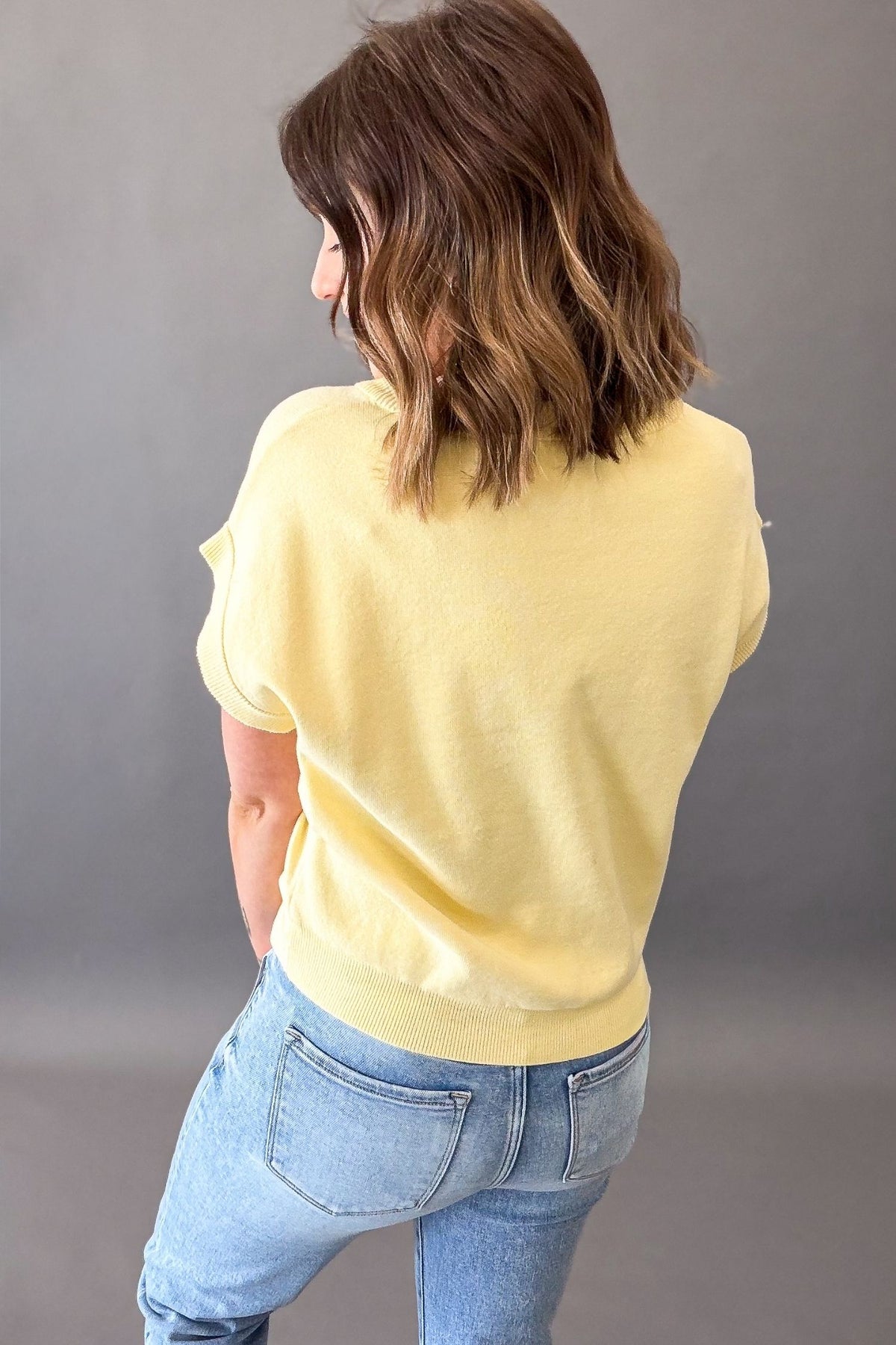 woman wearing a yellow button front cardigan with blue jeans on a grey background showing the back details