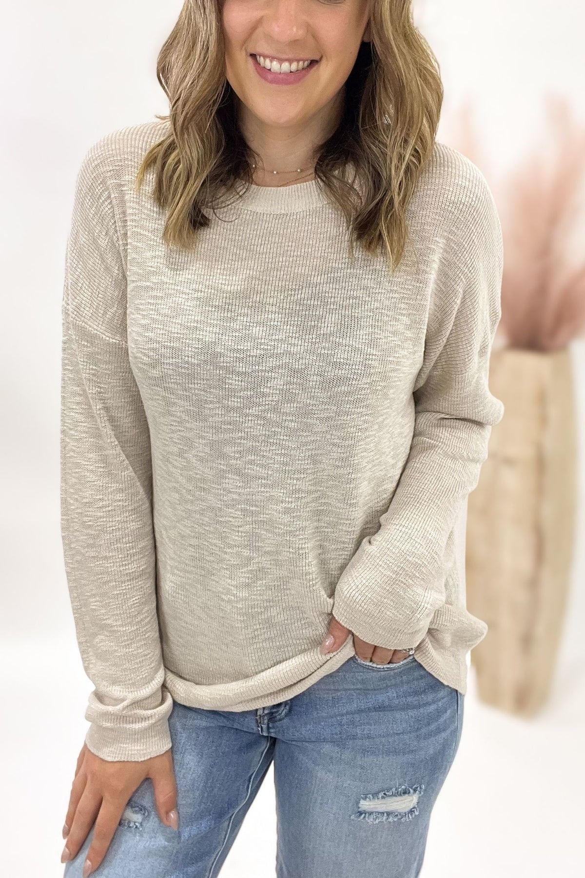Woman wearing a beige sweater and blue jeans with a white background