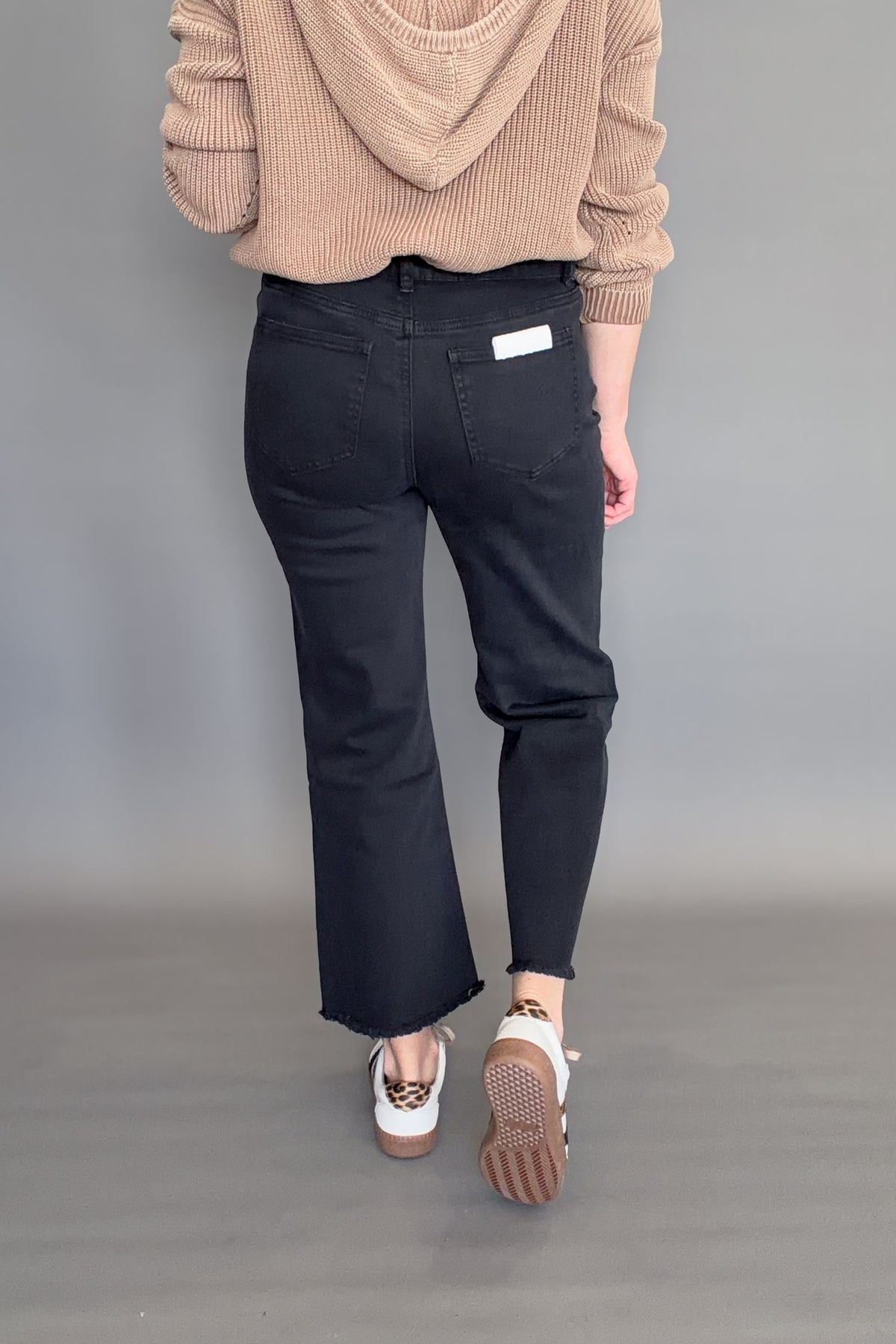 Back view of black high rise cropped bootcut jeans showing fitted waist, clean black wash, and raw hem detail.