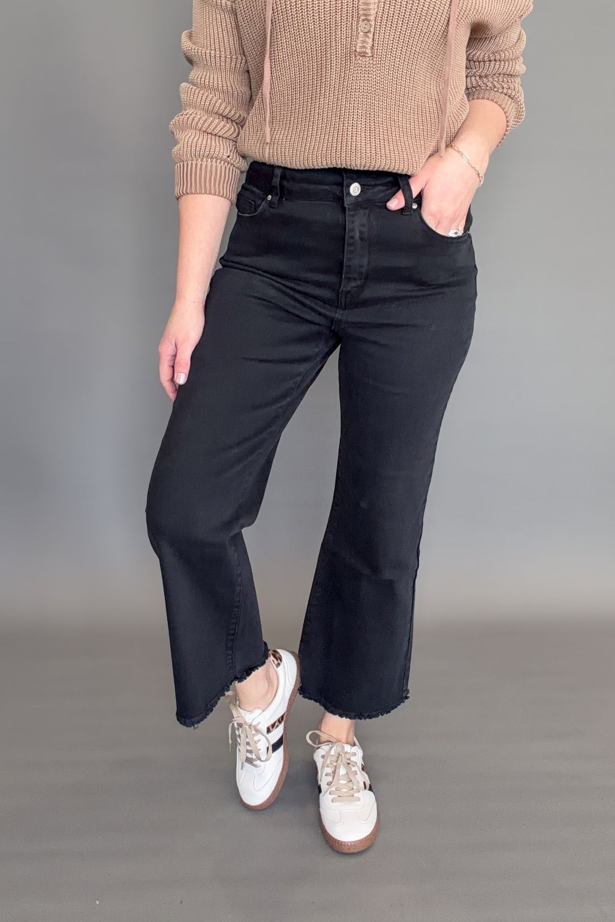 Black high rise crop bootcut jeans with frayed hem styled on model, front view with sneakers.